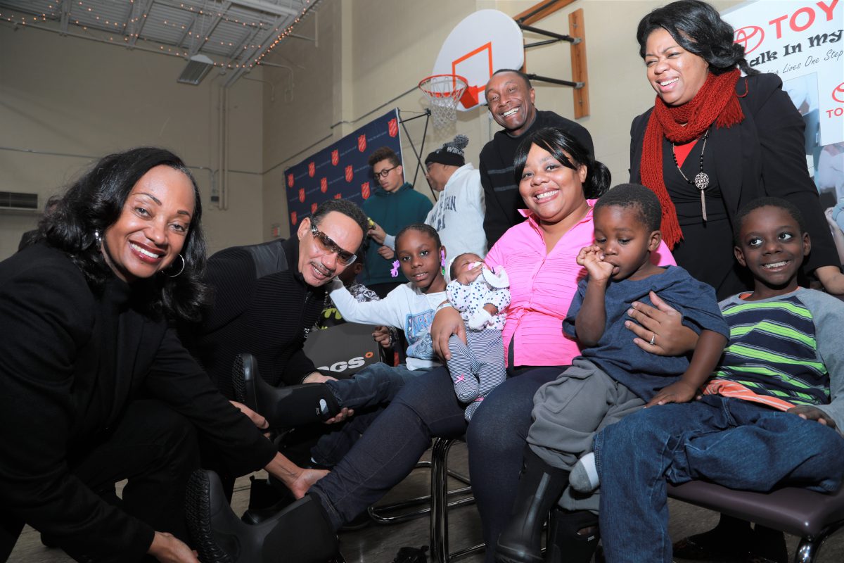 Photo credit:  Andrea Stinson-Oliver   Photo Caption:  Toyota Donates Winter Boots and Socks to Detroit Families In Need – NAIAS (Alva Mason, Toyota, Ronnie McNeir of The Four Tops, Greg Jackson, owner Prestige Warren Toyota and Kyra from TSA Booth Shelter help families try on new boots.)
