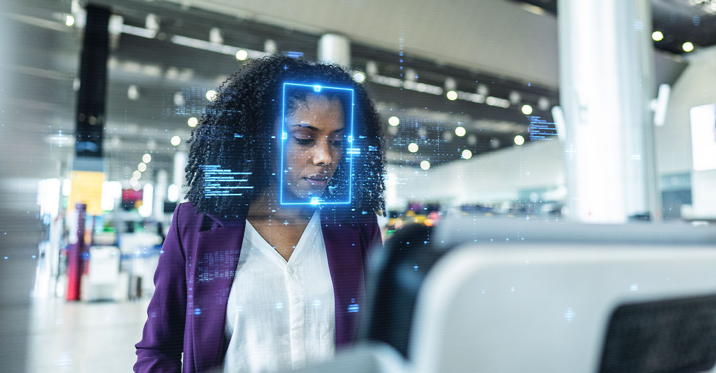 Focused young businesswoman standing at an airport check-in kiosk, with facial recognition technology digitally scanning her face, highlighting advanced security, innovation, and efficiency in modern travel.Focused young businesswoman standing at an airport check-in kiosk, with facial recognition technology digitally scanning her face, highlighting advanced security, innovation, and efficiency in modern travel.