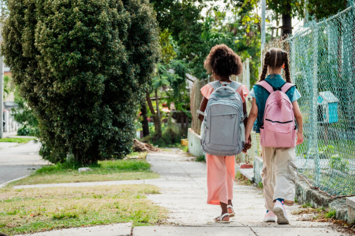 Child girls walking hand in hand to school outdoors